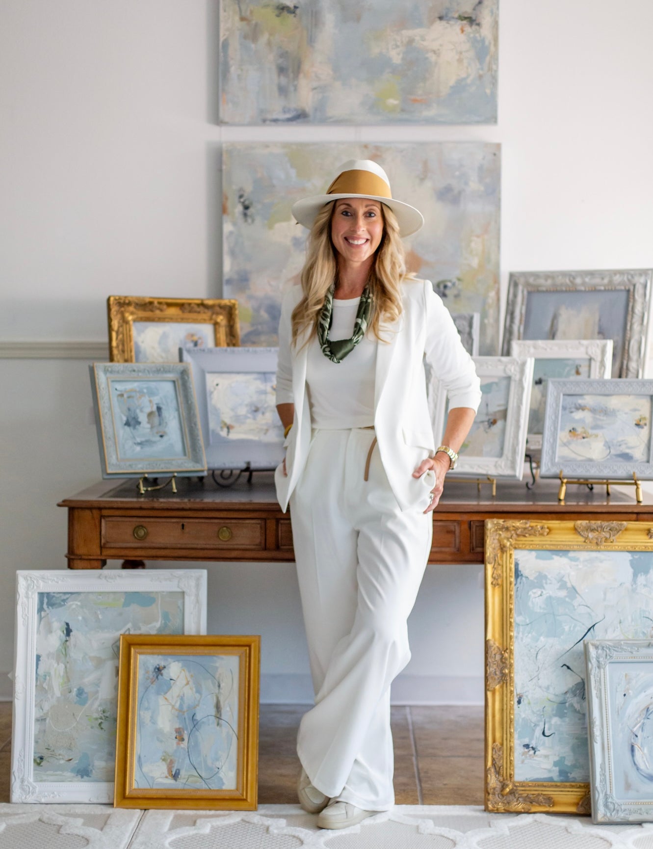 Woman in a white outfit standing in a room with framed artworks on a wall.