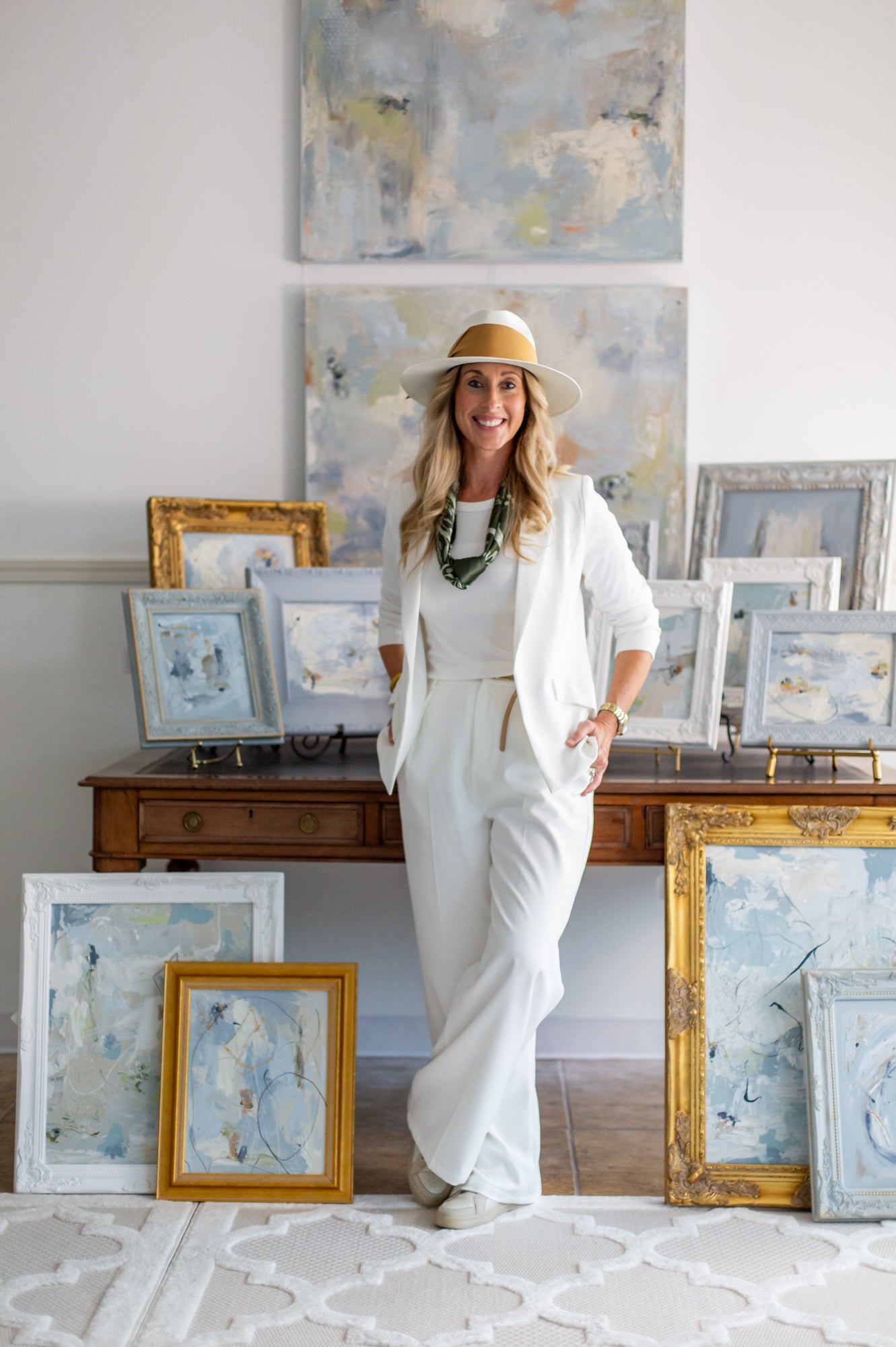 Woman in a white outfit standing in a room with framed artworks on a wall.